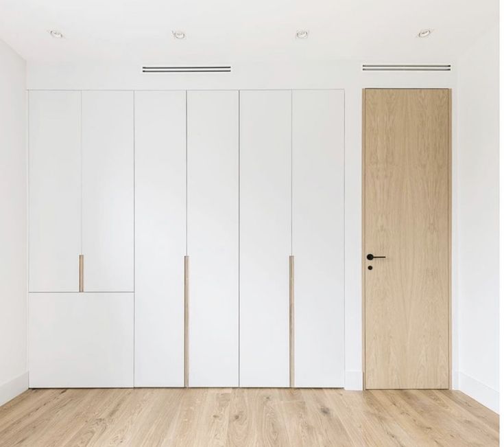 an empty room with white closets and wood flooring is seen in this image