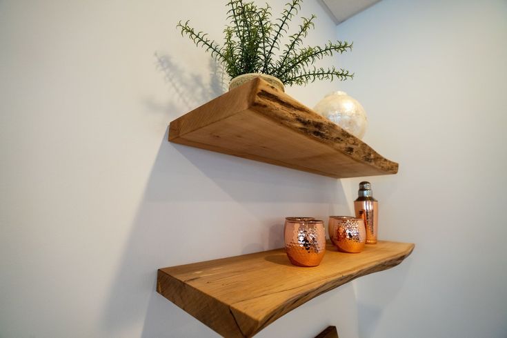 two wooden shelves with vases and candles on them against a white wall in a room