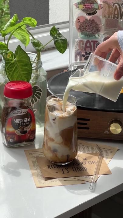 a person pouring milk into a glass on top of a table next to plants and other items