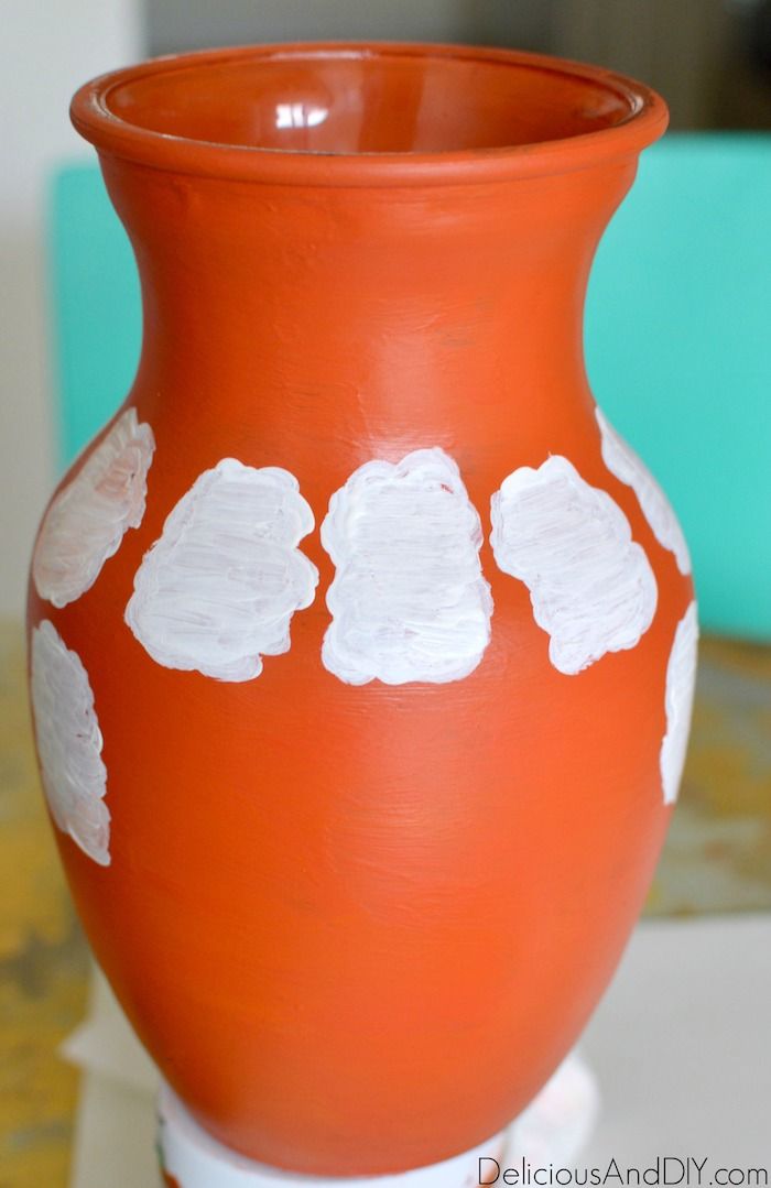 an orange vase with white flowers painted on it