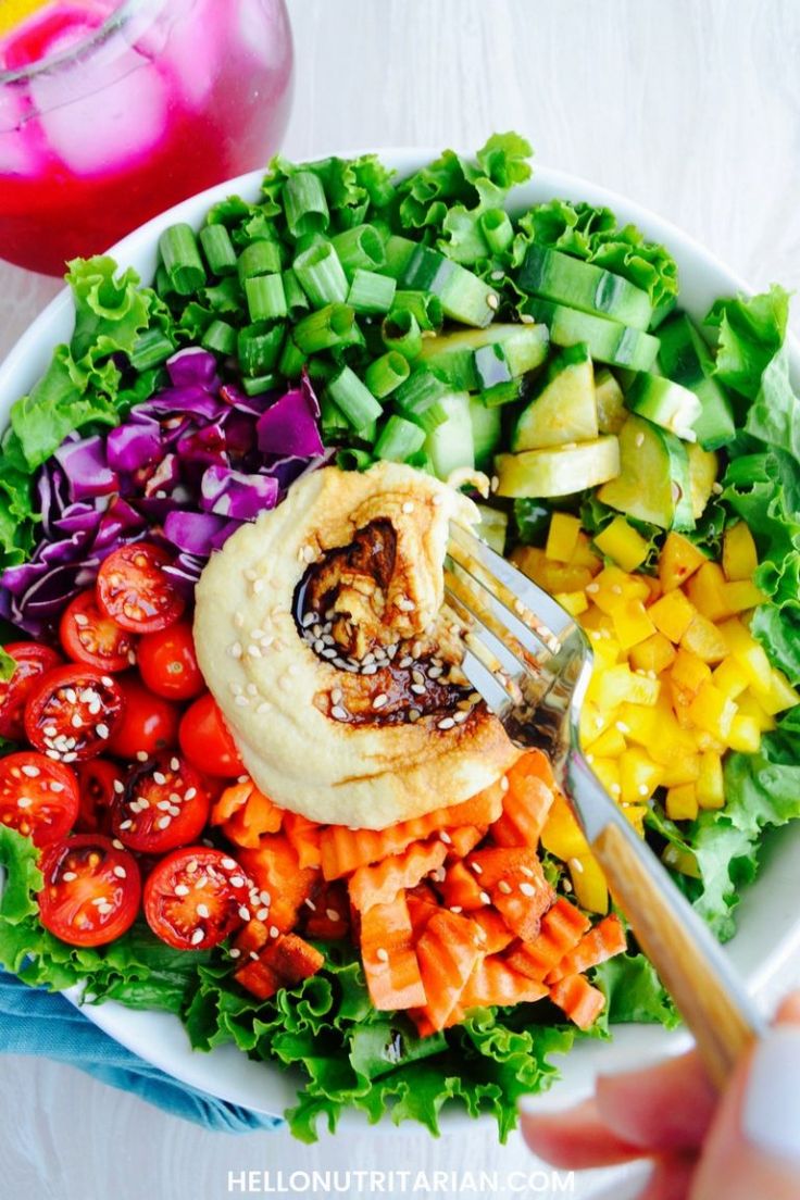 a person holding a fork over a salad with pita bread and vegetables on it