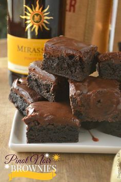 chocolate brownies on a white plate with a bottle of wine in the back ground