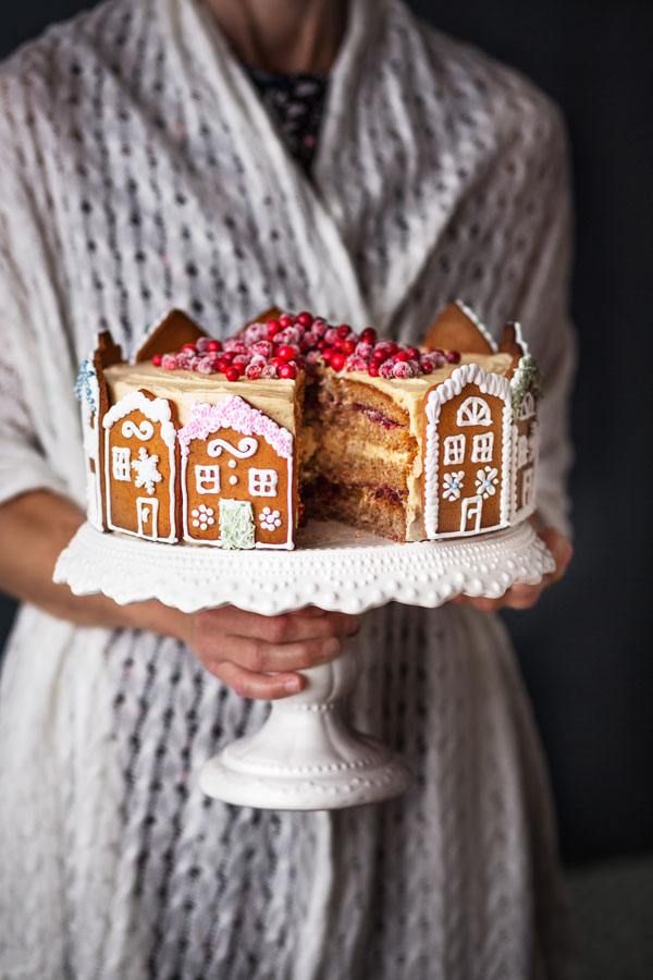 a woman holding a cake with gingerbread houses on it