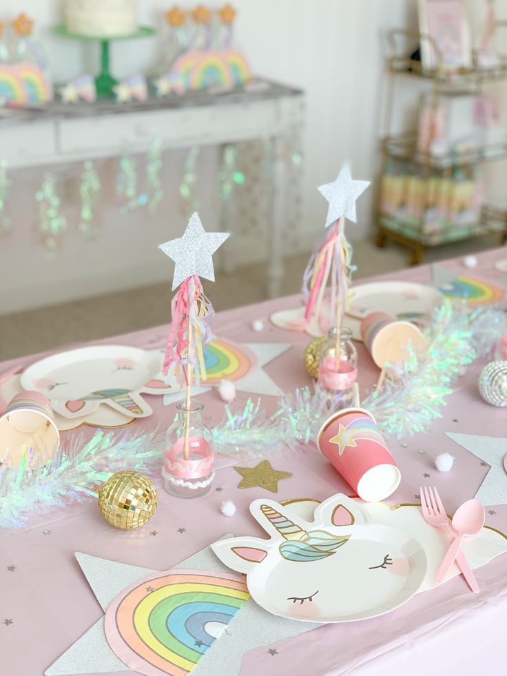 a table topped with lots of pink and white plates covered in unicorn themed paper decorations