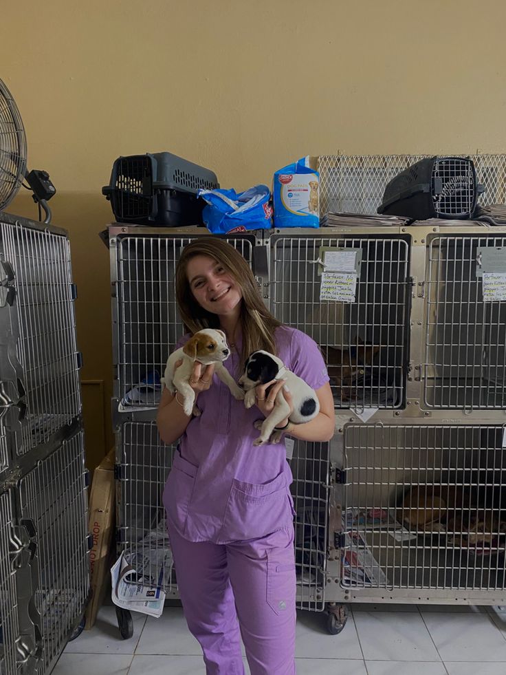 a woman in scrubs holding two puppies