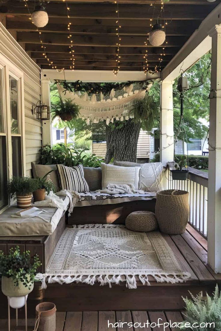 a porch covered in lots of plants and pillows with lights hanging from the ceiling above it