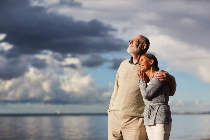 an older man and woman standing next to the ocean