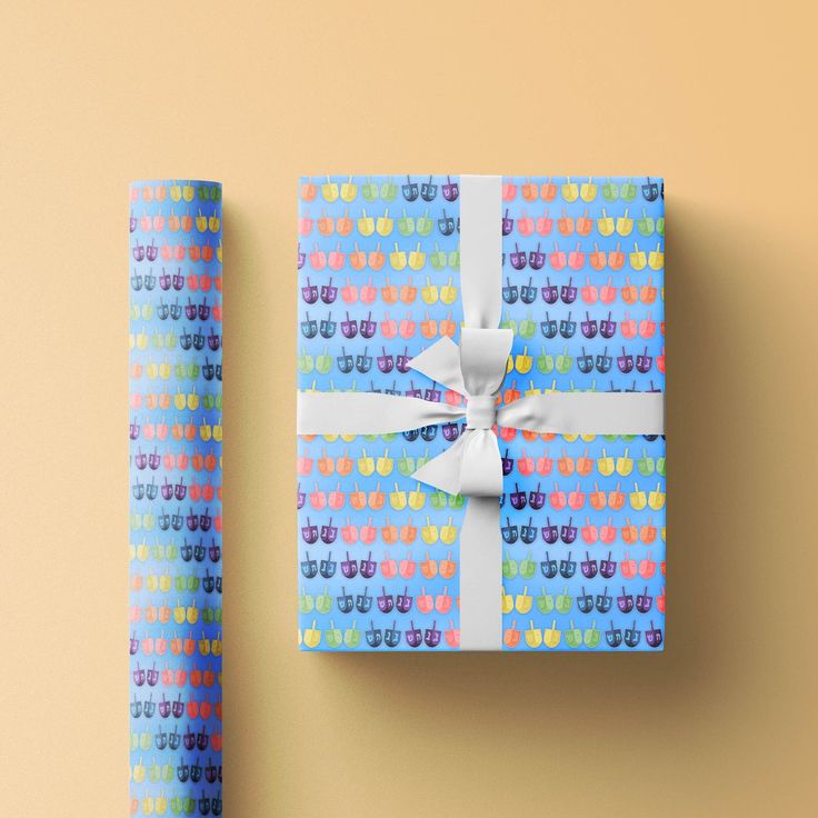 a present wrapped in blue and pink paper with a white bow on the top, next to a roll of wrapping paper