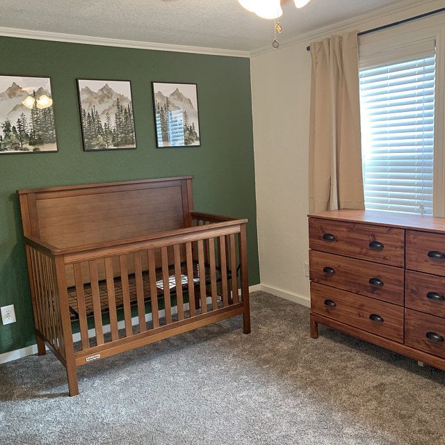 a baby crib and dresser in a room with green walls, two pictures on the wall