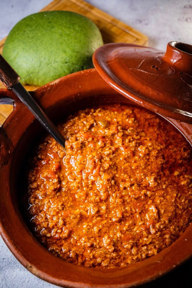 a wooden bowl filled with chili next to a lime