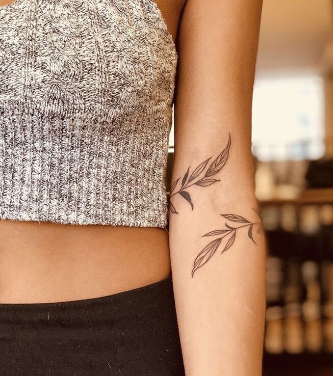 a close up of a person with a tattoo on their arm and behind her is a bar