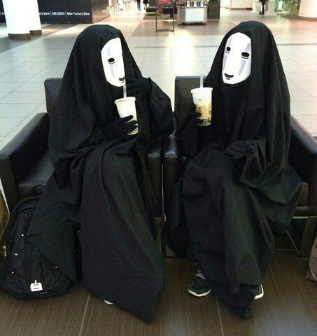 two people in black robes with masks on their faces, one holding a drink and the other wearing a mask