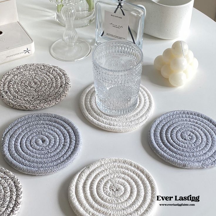 four coasters on top of a table next to a glass and candle holder with candles