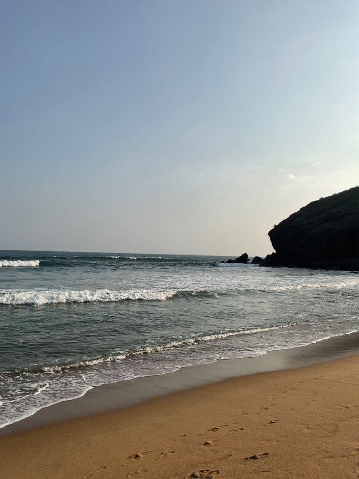 footprints in the sand on a beach with waves coming in to shore and a rock outcropping