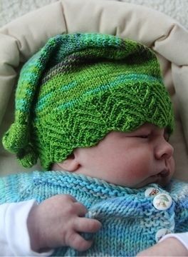 a baby wearing a green knitted hat and sleeping in a chair with its eyes closed