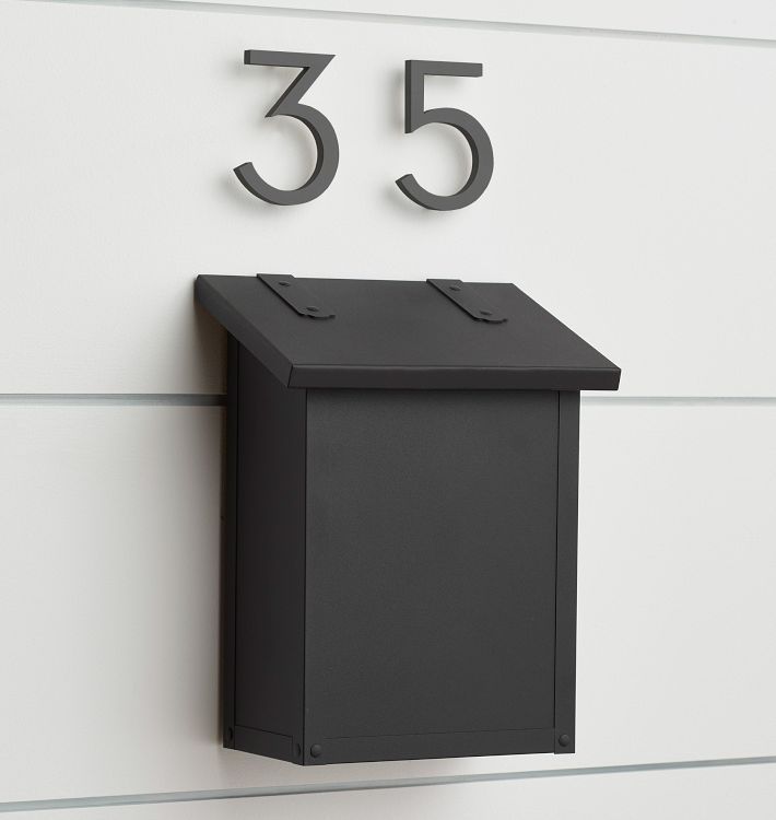 a black mailbox mounted to the side of a white wall with numbers on it