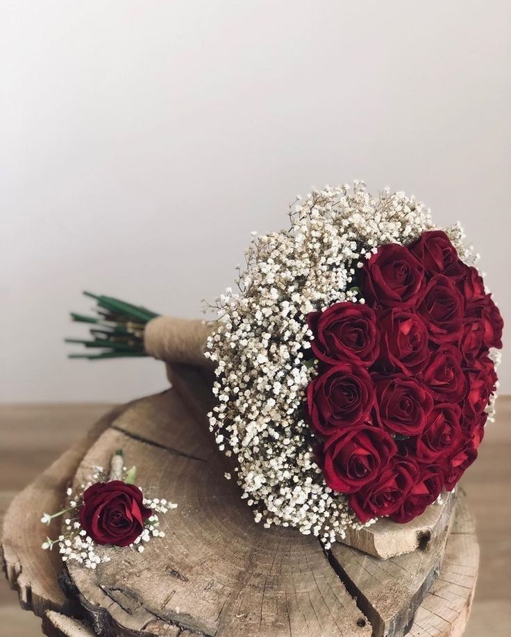 a bouquet of red roses and baby's breath on top of a piece of wood