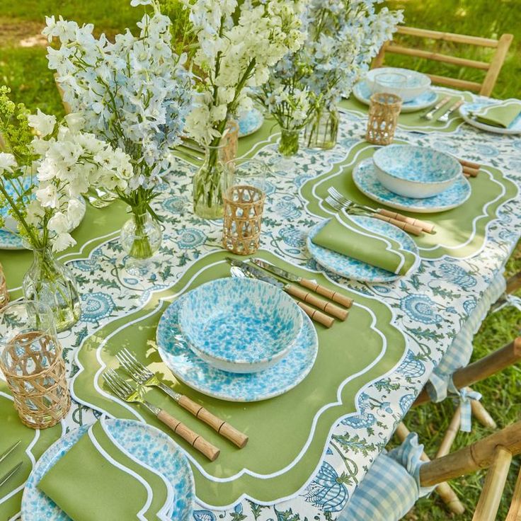 a table set with blue and white plates, napkins and flowers in vases