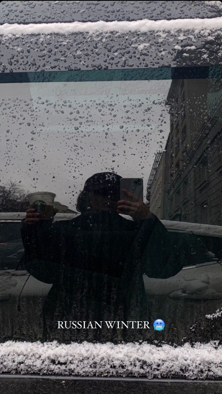 the reflection of a man holding a cup in front of his car's window