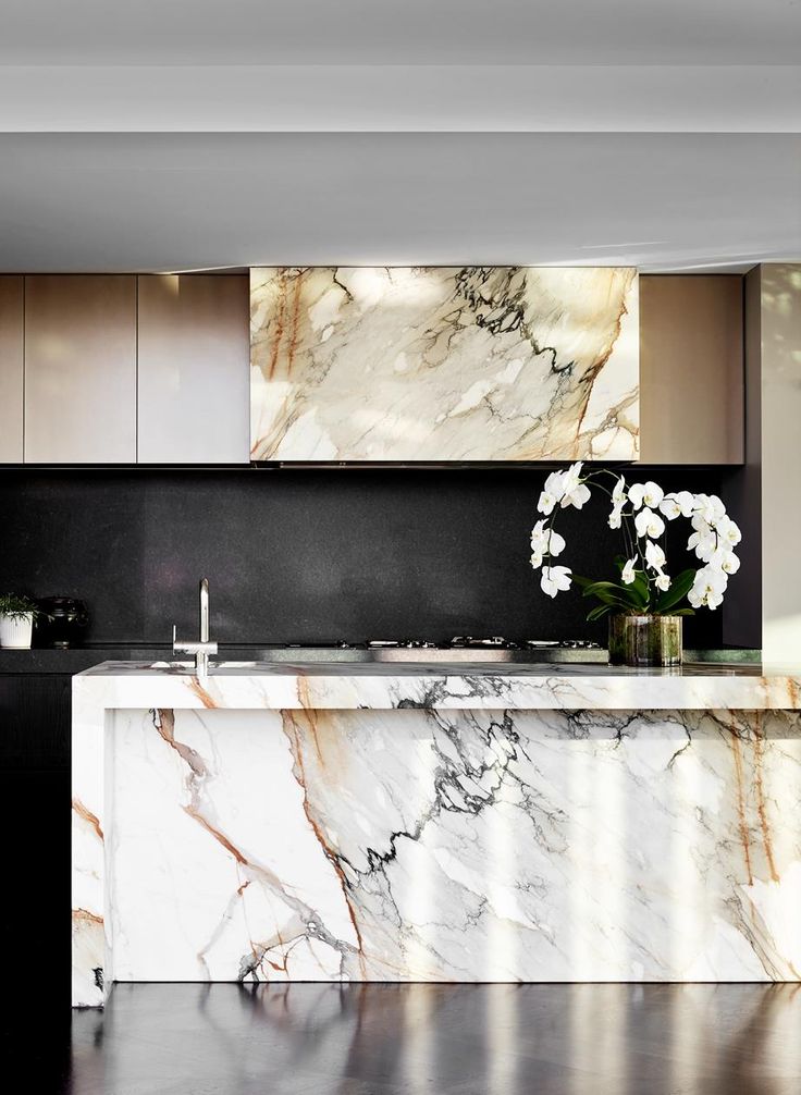 a kitchen with marble counter tops and white flowers in vases on the island top