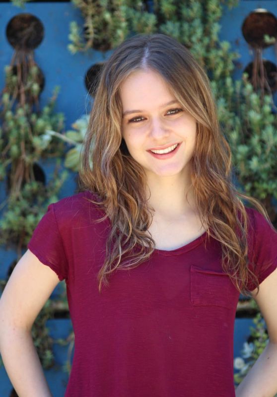 a young woman standing in front of a blue wall with plants growing on it's sides