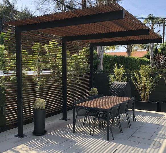 an outdoor dining area with wooden slatted walls and black metal chairs, table and potted plants