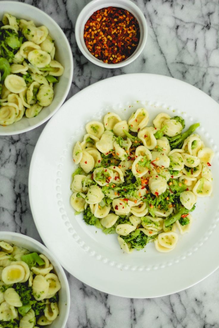 pasta with broccoli and other ingredients in bowls on a marble countertop top