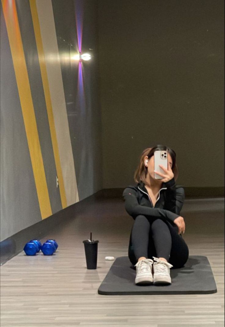 a woman taking a selfie with her cell phone while sitting on a yoga mat