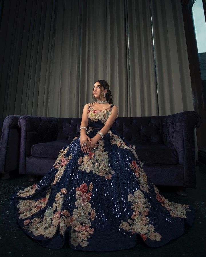 a woman is sitting on a couch in a blue dress with flowers and sequins