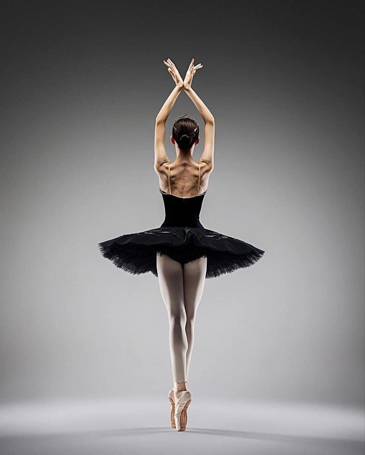 a ballerina in black leotard and tutu with her arms raised up