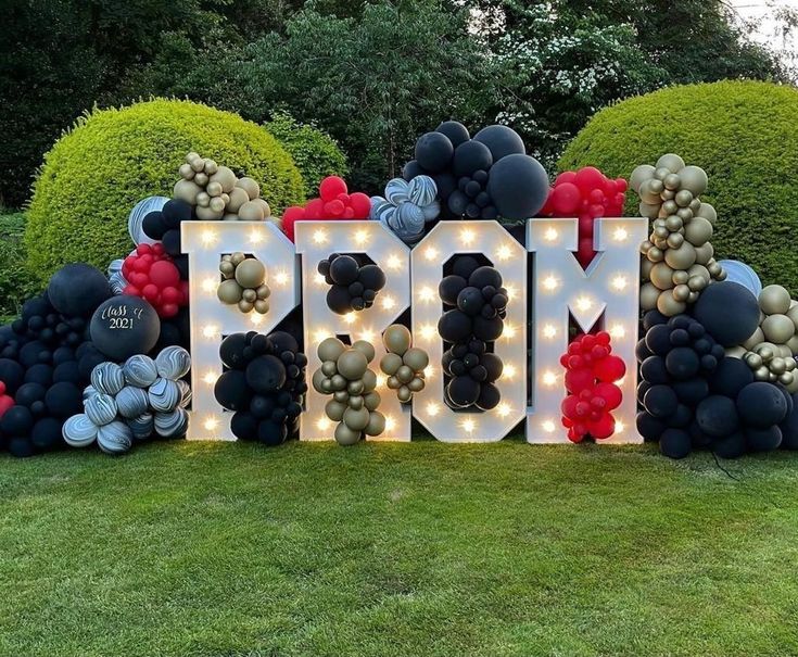 a large sign that says mom with balloons and lights on it in front of some bushes