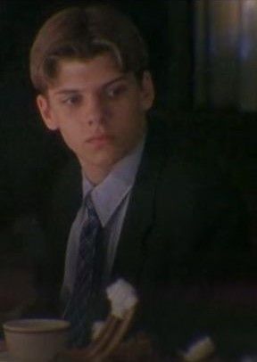 a young man in a suit and tie sitting at a table with a coffee cup