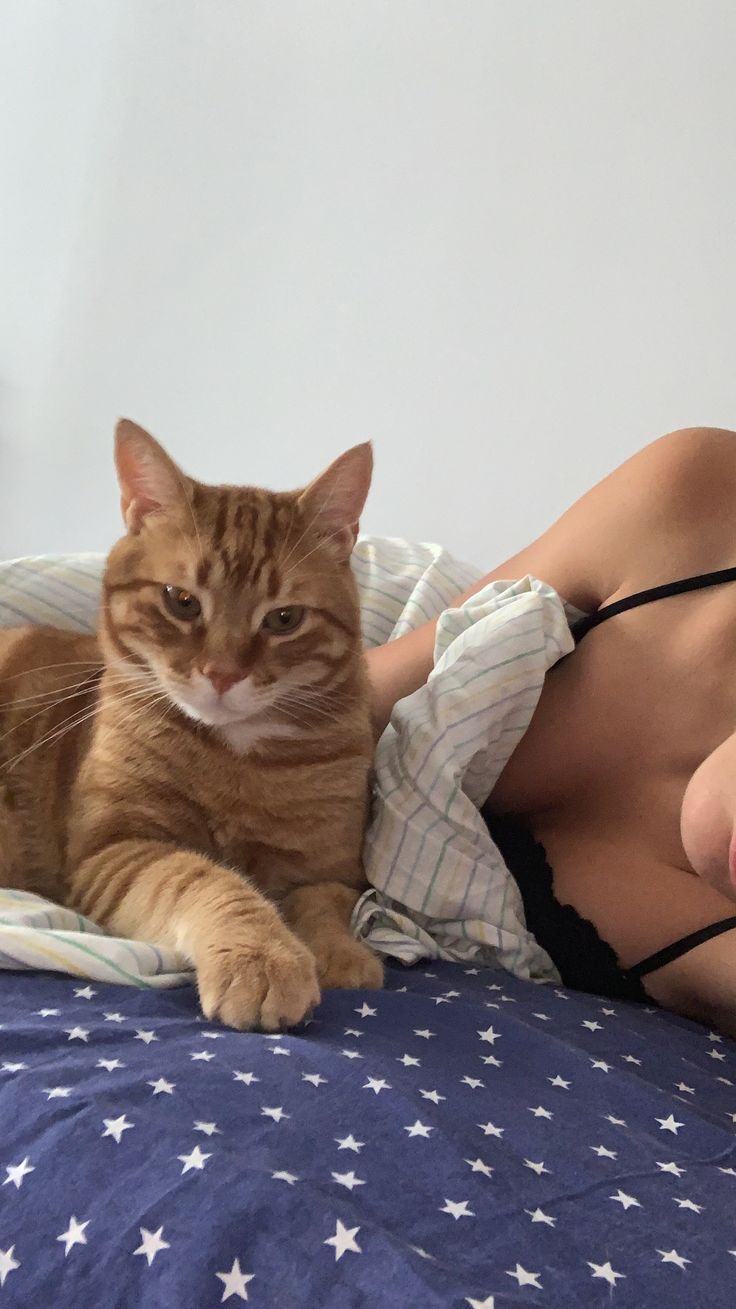 a woman laying on top of a bed next to an orange and white striped cat