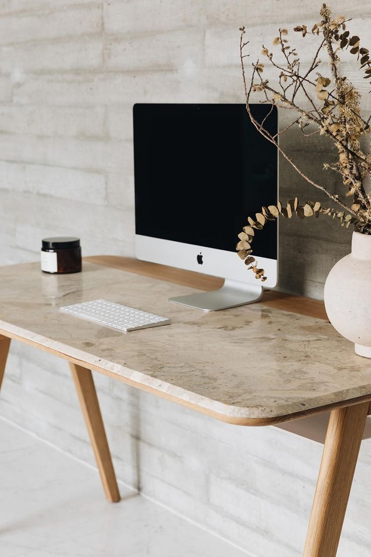 a computer monitor sitting on top of a wooden desk next to a vase filled with flowers