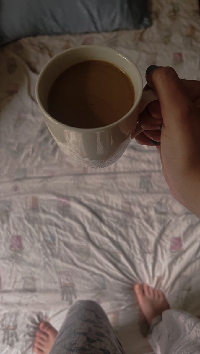 a person holding a cup of coffee on top of a bed