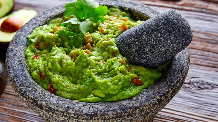 a mortar bowl filled with guacamole next to an avocado slice