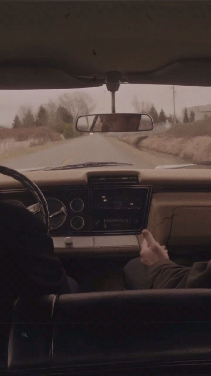 two people sitting in the driver's seat of a car on a country road