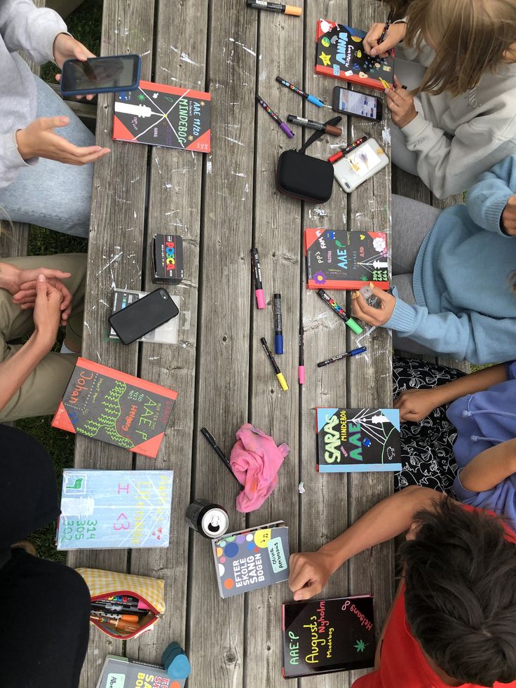 children are sitting at a picnic table and playing with their cell phones, notebooks and pens