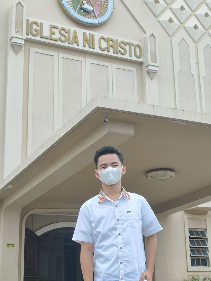 a man wearing a face mask standing in front of a building with an emblem on it