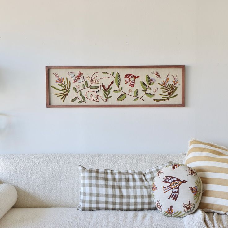 a white couch with pillows on it in front of a wall hanging above the couch