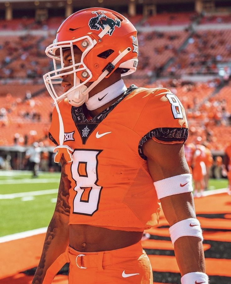 a football player wearing an orange uniform on the sidelines with his helmet in hand