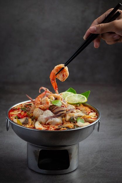 a person holding chopsticks above a bowl of food with shrimp and vegetables on it