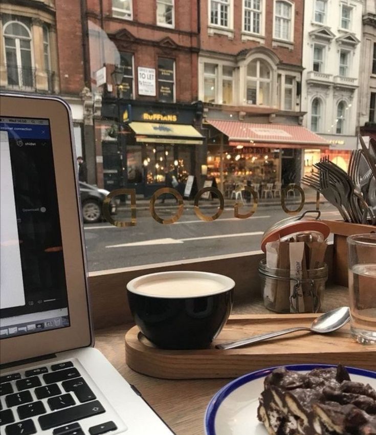 a laptop computer sitting on top of a table next to a cup of coffee and cake