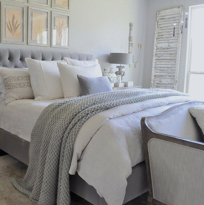 a bed with white sheets and pillows in a bedroom next to a window filled with pictures on the wall