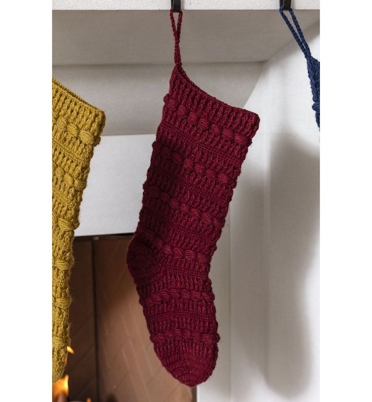 a red knitted stocking hanging from a hook on a wall next to a fireplace