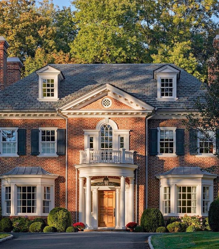 a large red brick house with white trim and black shutters on the front door