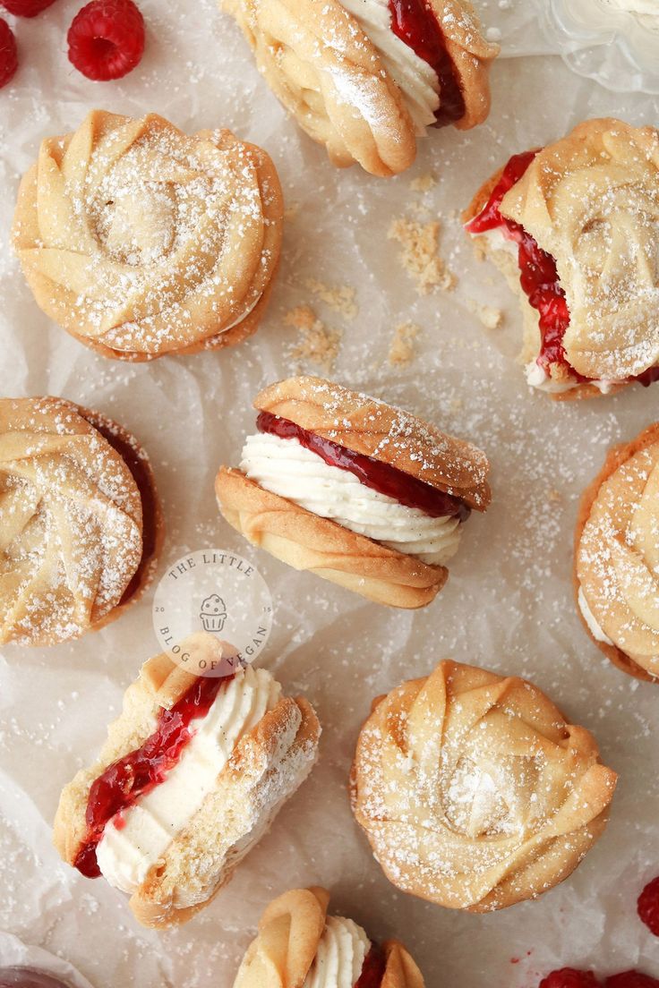 several pastries are sitting on wax paper with powdered sugar and raspberries