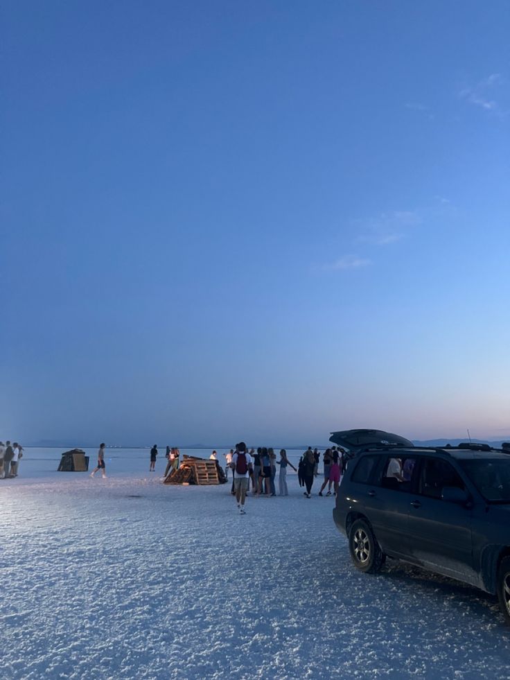 a group of people standing next to a parked car on top of snow covered ground