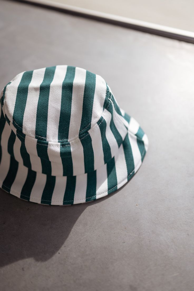 The hat is a stylish and comfortable accessory that is perfect for any casual outfit. Made from 100% cotton, it is breathable and soft to the touch. The green and white lines add a pop of color and a touch of personality, making it a unique and eye-catching piece. Matching set: Green Striped Denim Effect Kalina Shirt Green And White Striped Bucket Hat, White Cotton Summer Hat, White Cotton Summer Sun Hat, White Cotton Bucket Hat For Summer, Trendy Cotton Sun Hat With Flat Brim, White Cotton Bucket Hat For Vacation, White Cotton Vacation Hat, White Cotton Bucket Hat One Size, White Cotton Brimmed Sun Hat