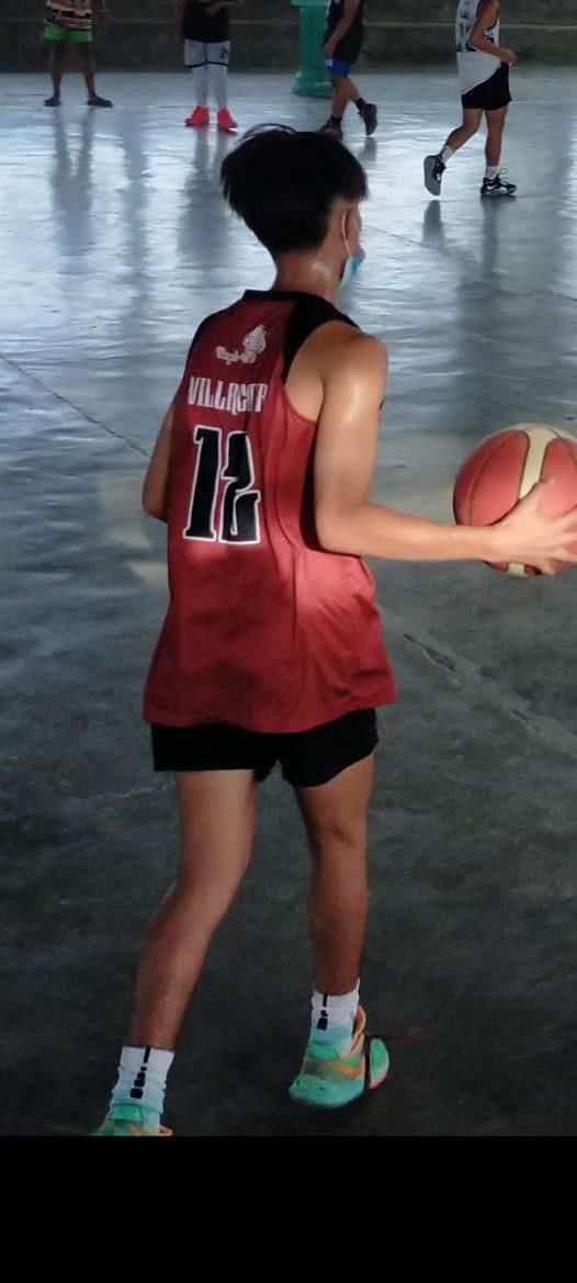 a man holding a basketball in his right hand while wearing a red jersey and black shorts